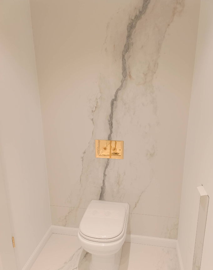 Gäste-WC mit durchgehend gefliester Wand in Marmoroptik und goldener Betätigungsplatte